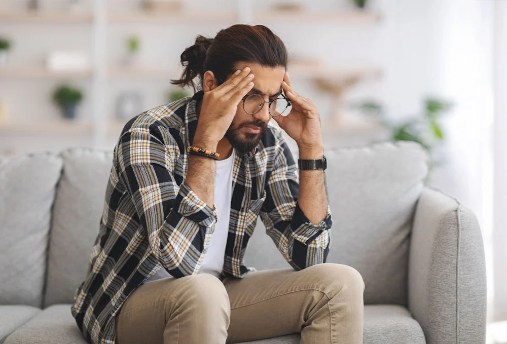 man sitting on couch showing visible signs of anxiety struggle